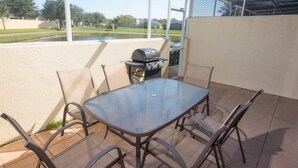 An outdoor patio with a glass table and chairs, a grill, and a view of a park and lake.