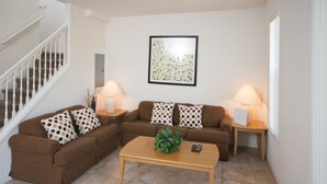 A living room with a brown sectional sofa, two side tables with lamps, a coffee table with a plant, and a framed artwork on the wall.