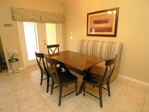 A dining area with a wooden table and four chairs, a striped bench, and a framed picture on the wall.