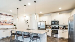 Una cocina moderna con una isla central, electrodomésticos de acero inoxidable e iluminación colgante.