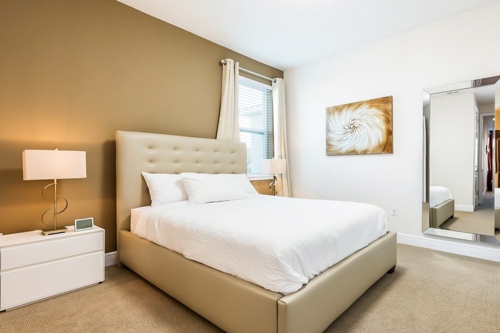 Una camera d'albergo moderna con un letto grande, un comodino con una lampada, uno specchio e un quadro appeso al muro.