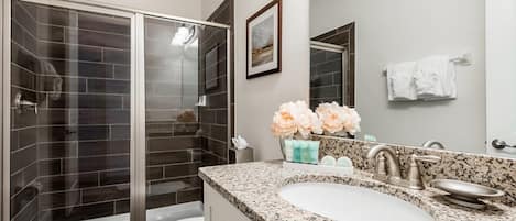 A modern bathroom with a glass-enclosed shower, a white toilet, a granite countertop sink, and a mirror above the sink.