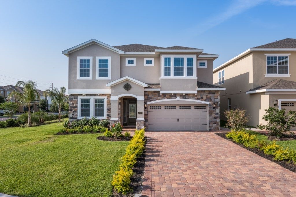 A two-story house with a brick driveway, a garage, and a well-maintained lawn.