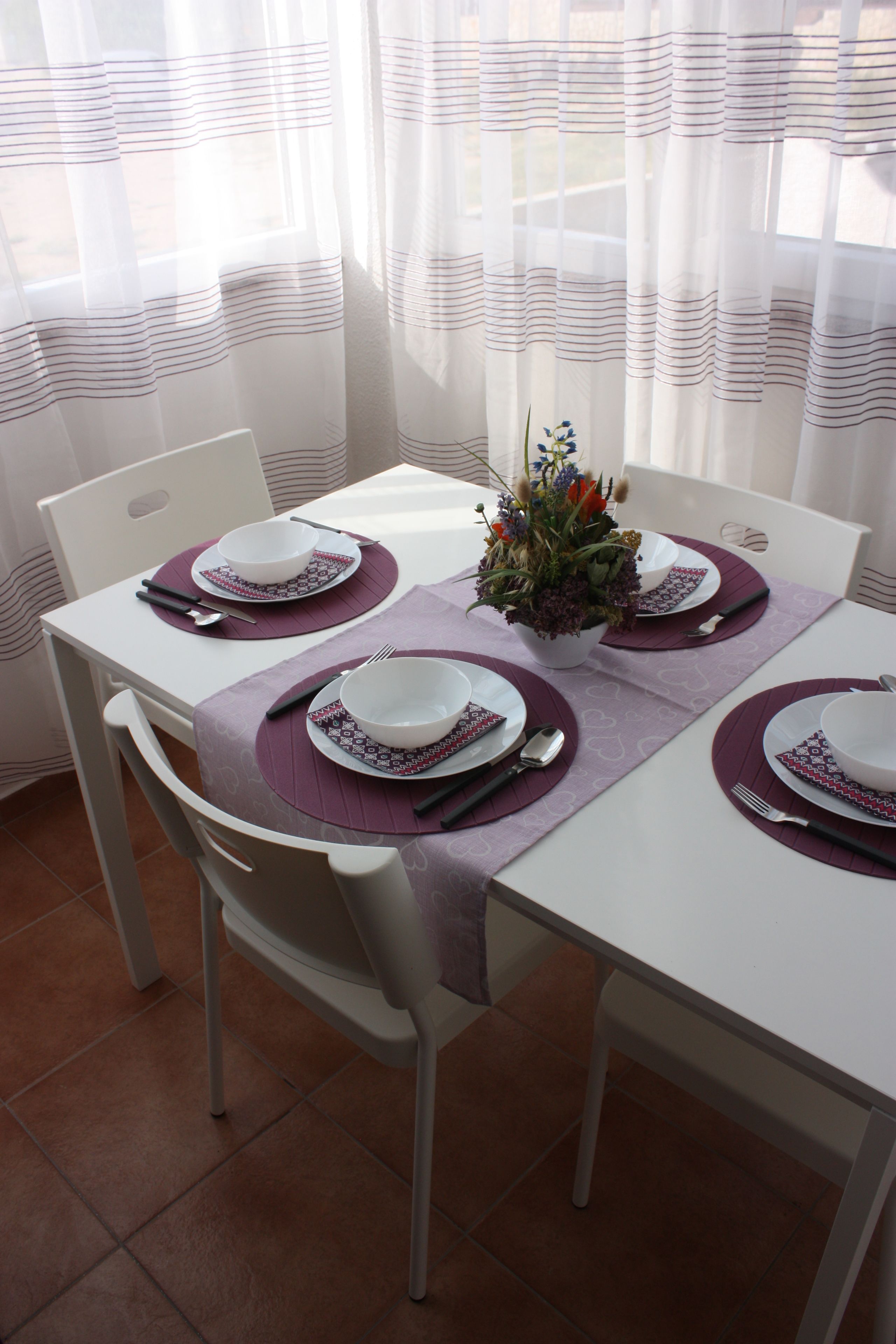 A dining table set with white plates, purple placemats, and a floral centerpiece.