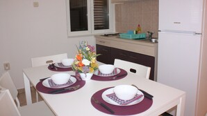 A dining table set for four with white plates, purple placemats, and a vase of flowers. - Apartments Blato-M (Pag)