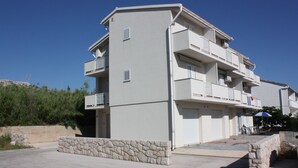 A multi-story building with balconies, a stone wall in front, and a clear blue sky. - Apartments Blato-M (Pag)