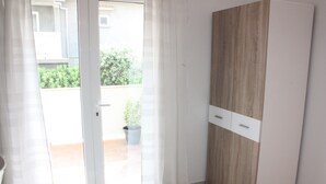 A room with a sliding glass door leading to a balcony, a wooden wardrobe, and a potted plant on the balcony. - Apartments Blato-M (Pag)
