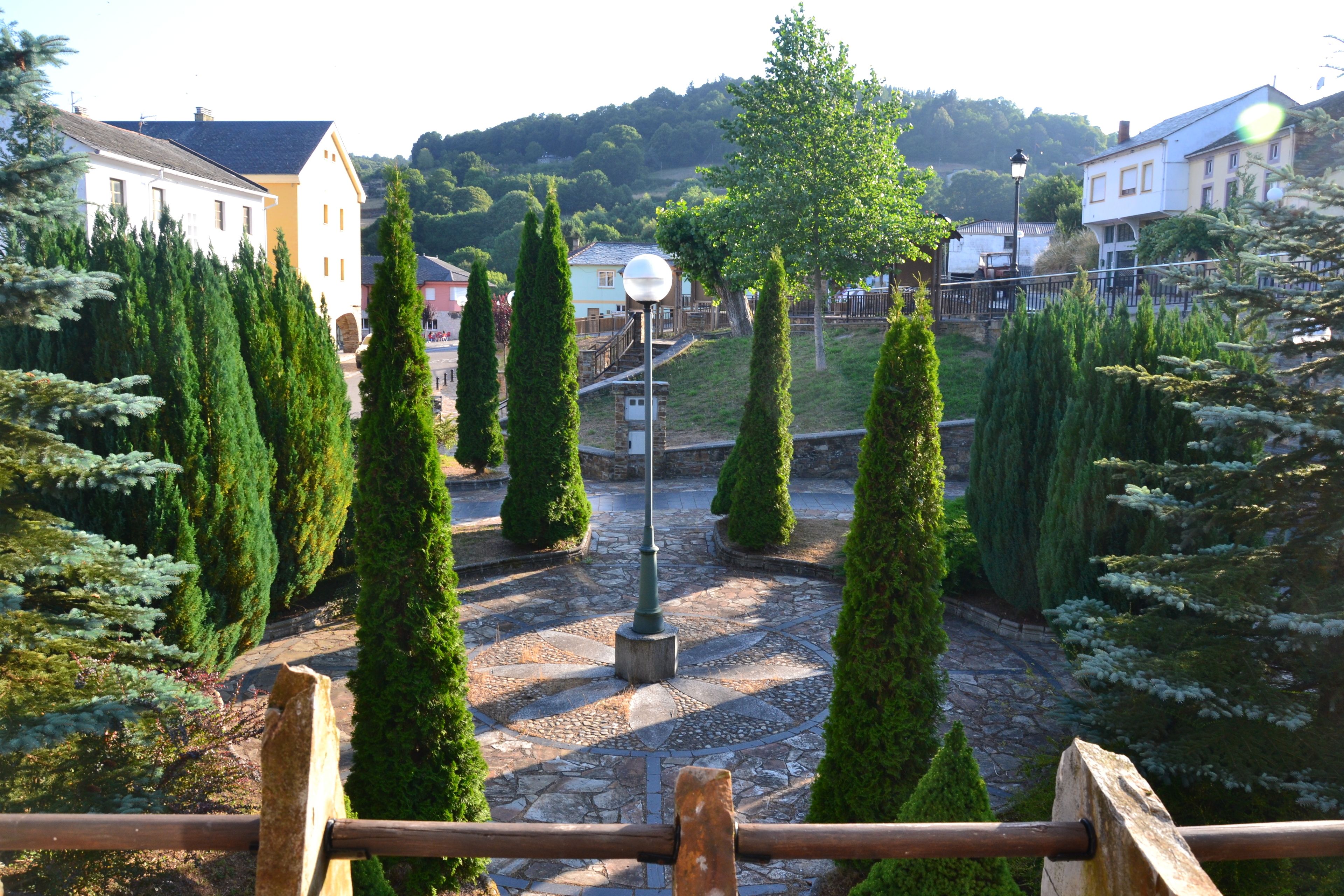 Un patio con pavimento de piedra, altos cipreses y un farol en el centro.