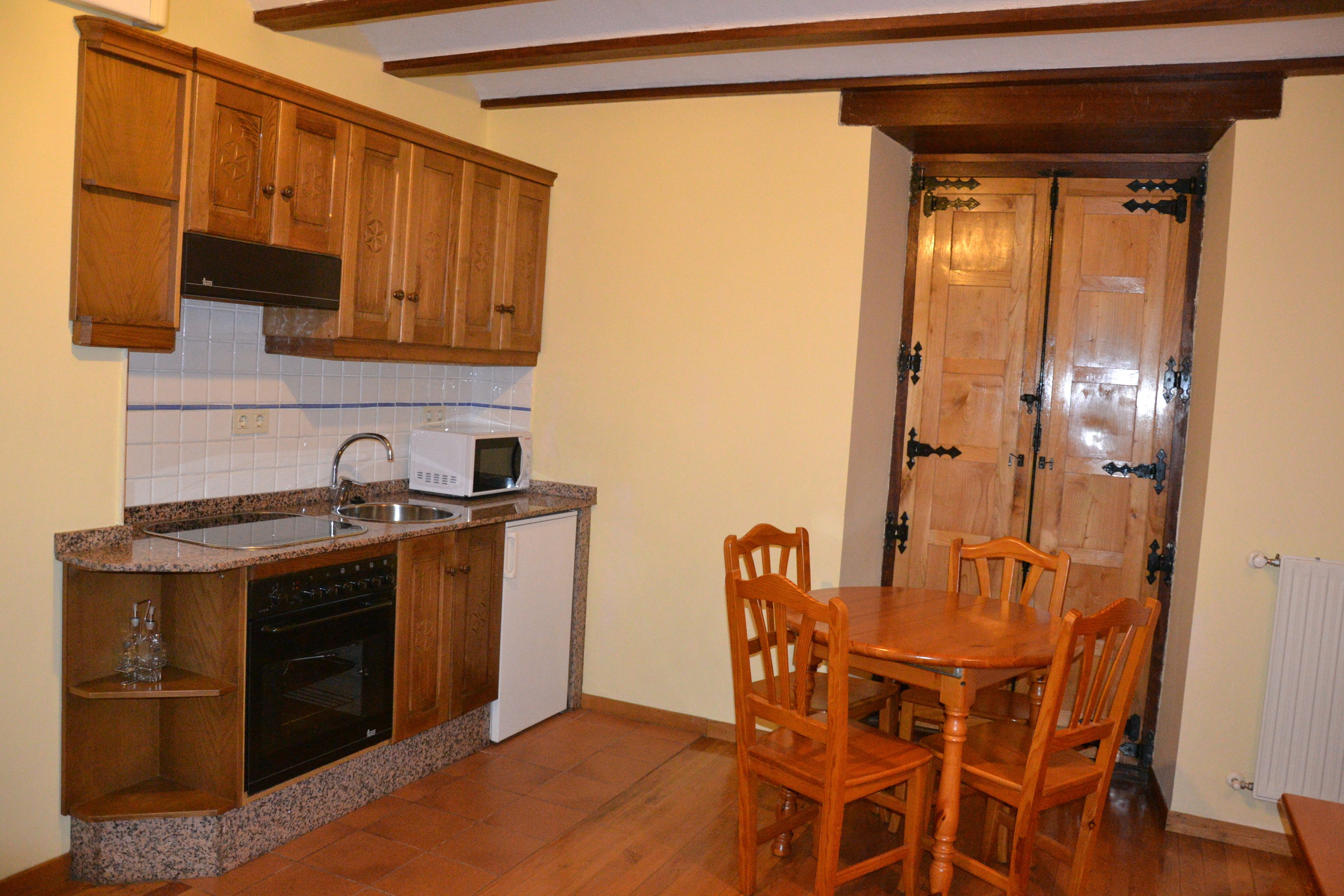 Una cocina con armarios de madera, horno empotrado, microondas y una mesa de comedor con sillas.
