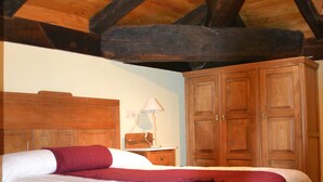 Een slaapkamer met een houten plafond, een bed met witte en bordeauxrode beddengoed, een nachtkastje met een lamp en een kledingkast.