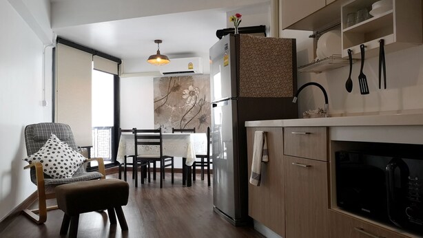 A modern kitchen with wooden cabinets, a dining area with a table and chairs, and a large window providing natural light. - Aunny House (Bangkok)