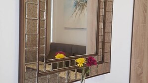A mirror with a geometric frame, a wooden console table with a black top, and a vase with flowers. - Aunny House (Bangkok)