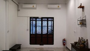 A spacious room with a large decorative door, air conditioning units, a fire extinguisher, and a small shelf with decorative items. - Aunny House (Bangkok)