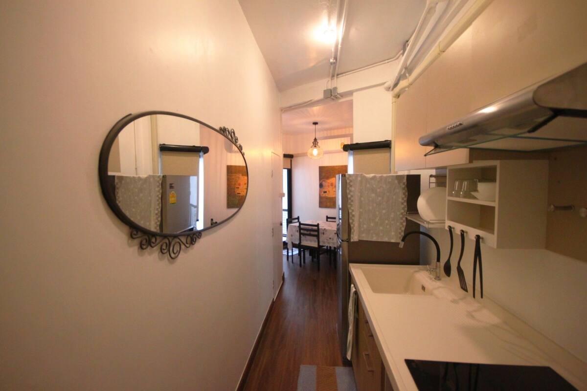 A narrow hallway leading to a kitchen area with a sink, utensils, and a mirror.