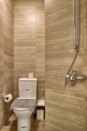 A bathroom with beige tiles, a toilet, a shower, and a towel on the toilet.