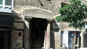 A building entrance with a metal gate, a bicycle parked outside, and a tree nearby. - Baratero City II Apartment (Sofia)