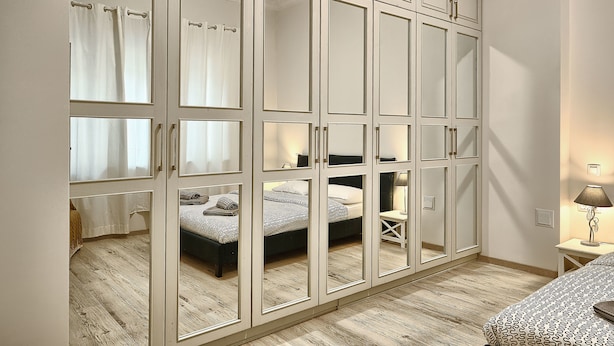 A bedroom with a large wardrobe, a bed, and a bedside table with a lamp. - Baratero City II Apartment (Sofia)