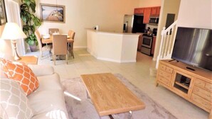 A living room with a sofa, coffee table, TV, and kitchen area with cabinets and appliances.