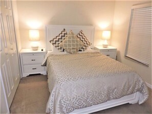 A bedroom with a patterned bedspread, two bedside lamps, a white headboard, and a window with blinds. - Aco225226 - Bella Vida Resort - 4 Bed 3 Baths Townhome (Kissimmee)