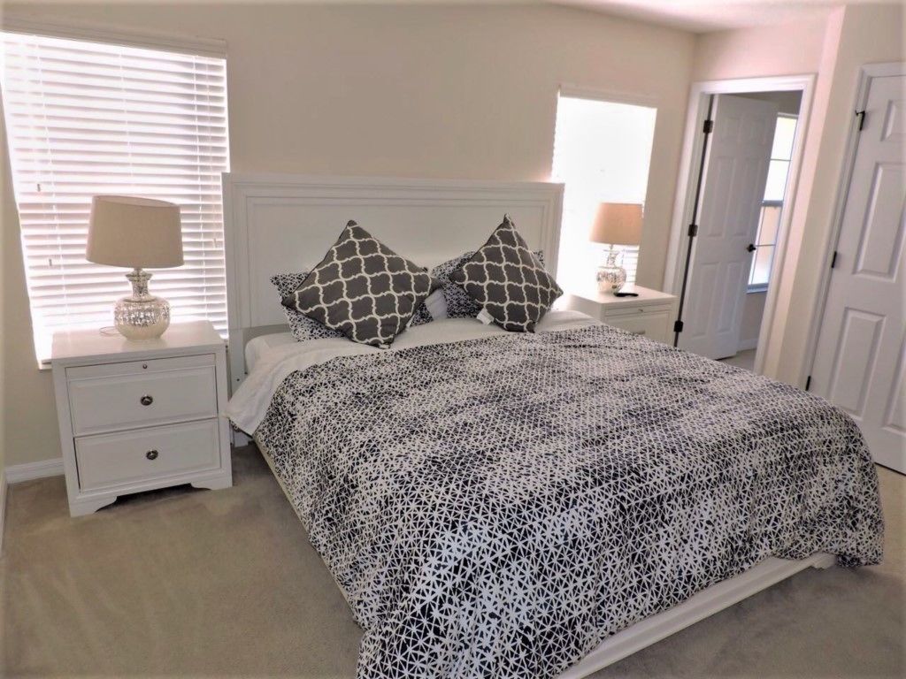 Une chambre à coucher avec un lit, deux tables de chevet, une fenêtre avec des stores et une porte.