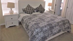 A bedroom with a bed, two nightstands, a window with blinds, and a door.