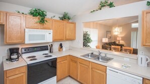 Cocina compacta con armarios de madera, microondas, estufa, fregadero y lavavajillas.