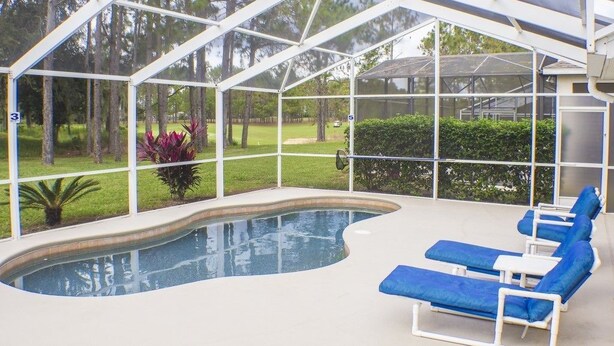 A covered swimming pool area with blue lounge chairs and a view of a golf course.