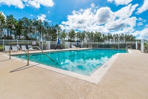 Une piscine dotée de chaises longues et entourée d’une clôture, le tout bordé d’arbres.