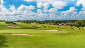 A golf course with bunkers, a flagstick, and a clear blue sky.