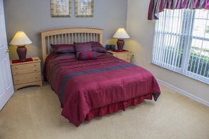 A bedroom with a bed, two bedside tables, a window with blinds, and two framed pictures on the wall.