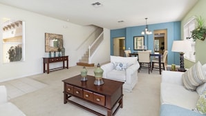A spacious living room with a staircase, a dining area, and a kitchen visible through an open door. - Aco243016 - Bella Vida Resort - 6 Bed 5.5 Baths Villa (Kissimmee)
