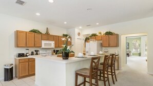 A modern kitchen with wooden cabinets, a central island, and a dining area with bar stools. - Aco243016 - Bella Vida Resort - 6 Bed 5.5 Baths Villa (Kissimmee)