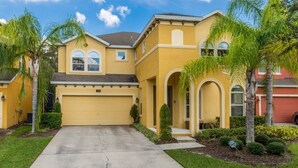 A yellow two-story house with a garage, palm trees, and a well-maintained lawn. - Aco243016 - Bella Vida Resort - 6 Bed 5.5 Baths Villa (Kissimmee)