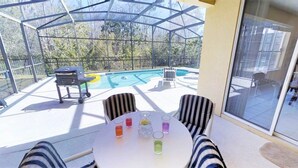 A covered outdoor area with a pool, a grill, and striped chairs around a table with drinks. - Aco243016 - Bella Vida Resort - 6 Bed 5.5 Baths Villa (Kissimmee)