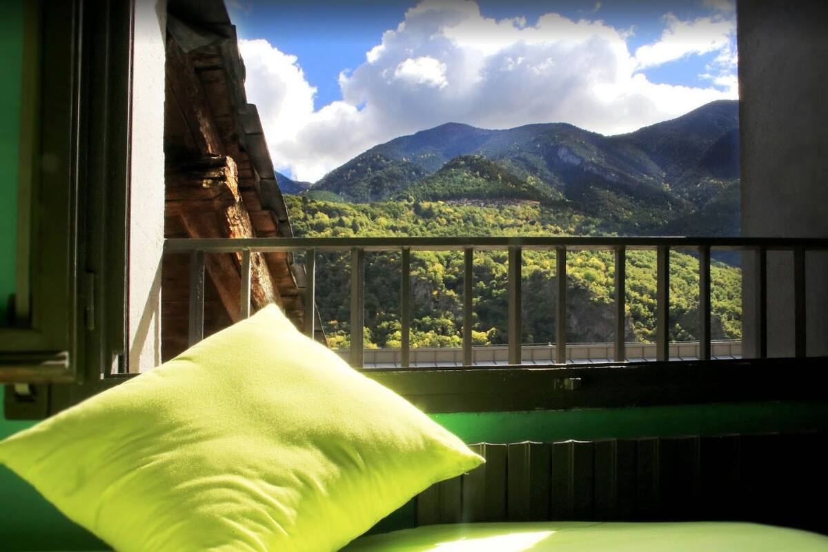 Quarto com vista para montanhas através de uma janela com grade de metal.