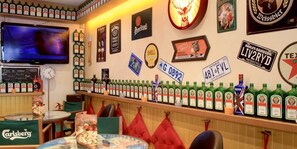 Un coin bar avec un assortiment de bouteilles d’alcool, un téléviseur et des objets de collection accrochés au mur.