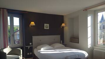 Et hotelværelse med en seng, to væglamper, et vindue med udsigt til en bygning og en stol.
