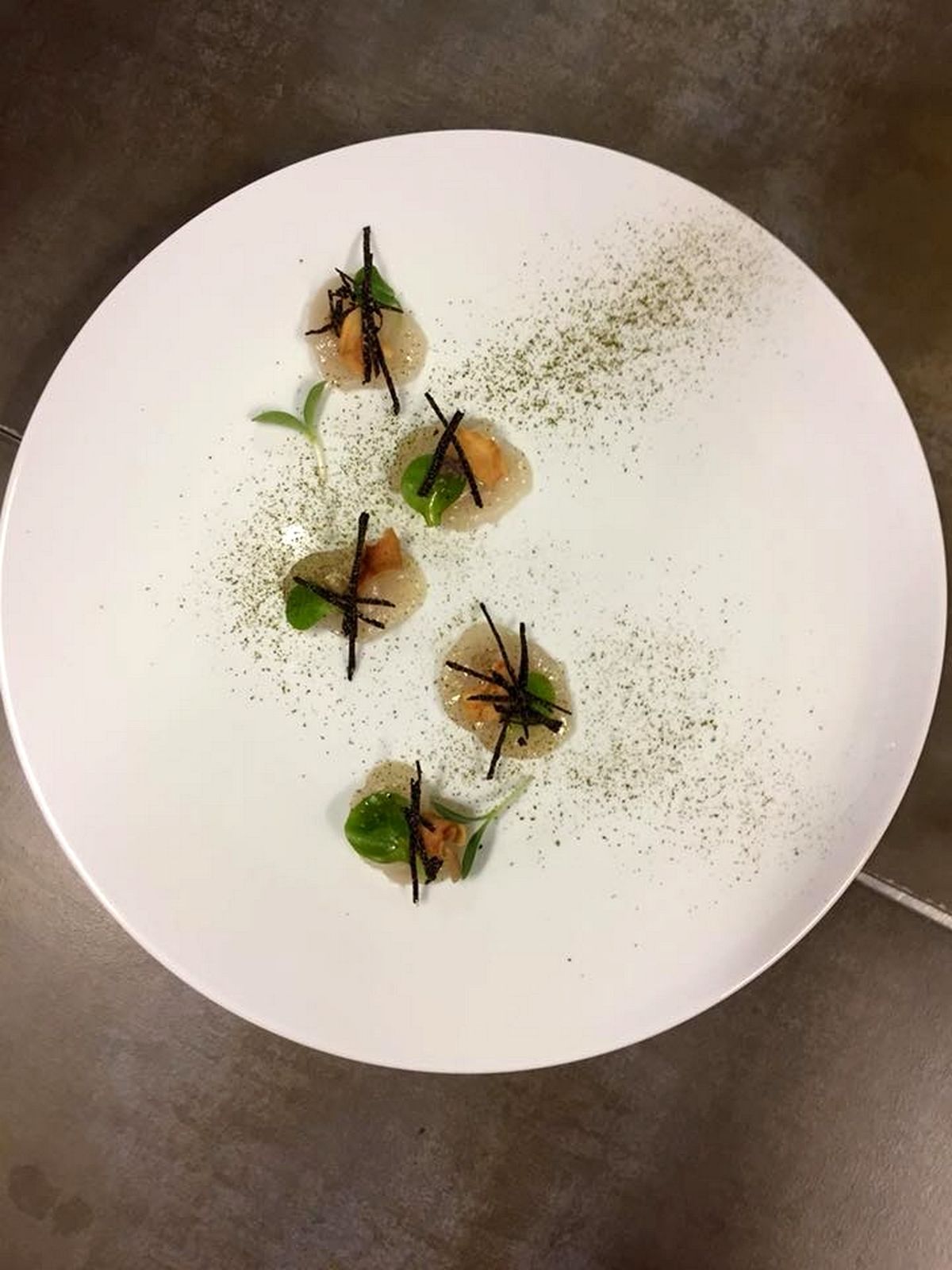 A white plate with four food items, each garnished with a green leaf and a black garnish, on a textured surface.