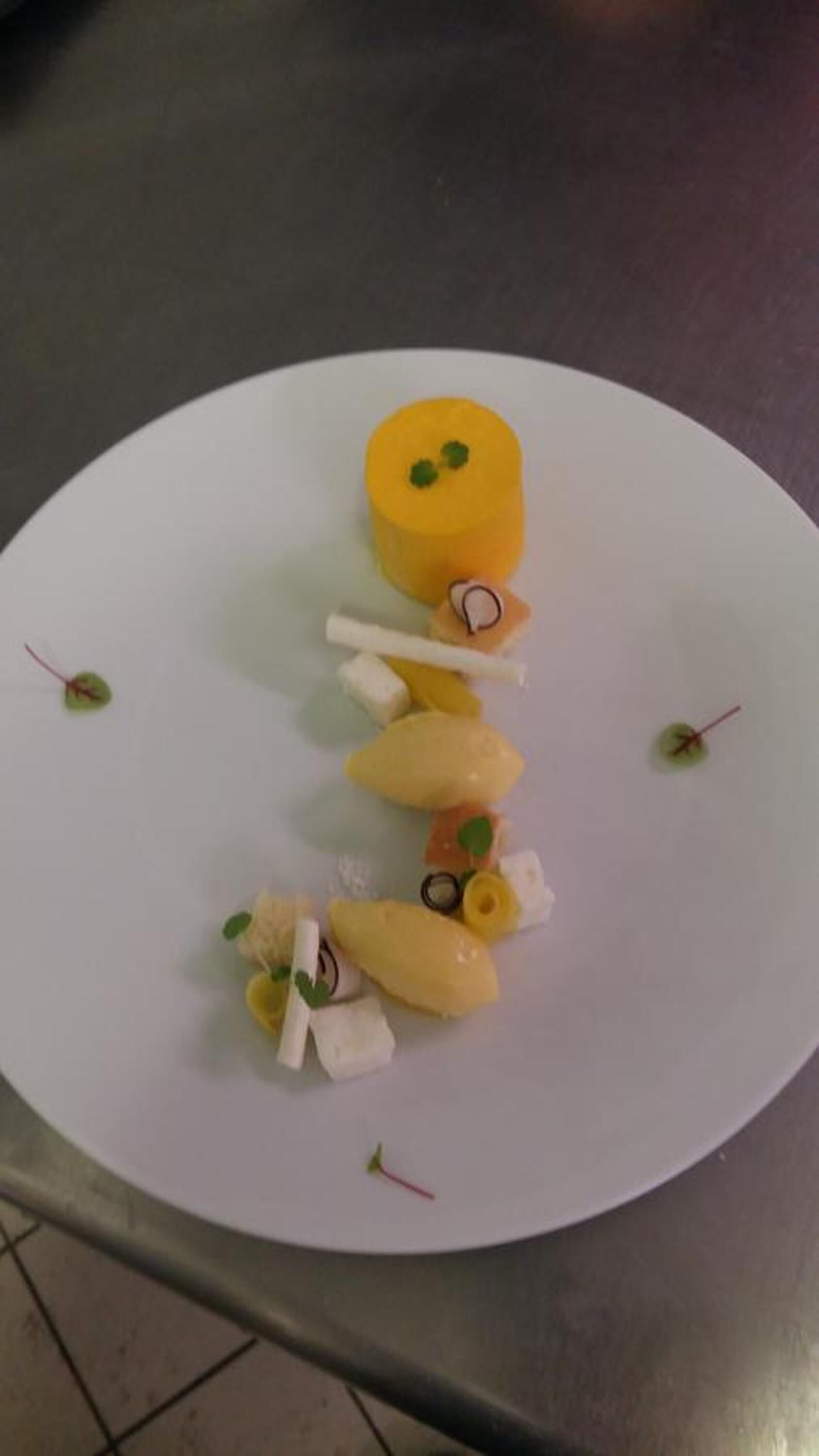 A white plate with a variety of food items, including a yellow cylindrical item, white cubes, and small garnishes.