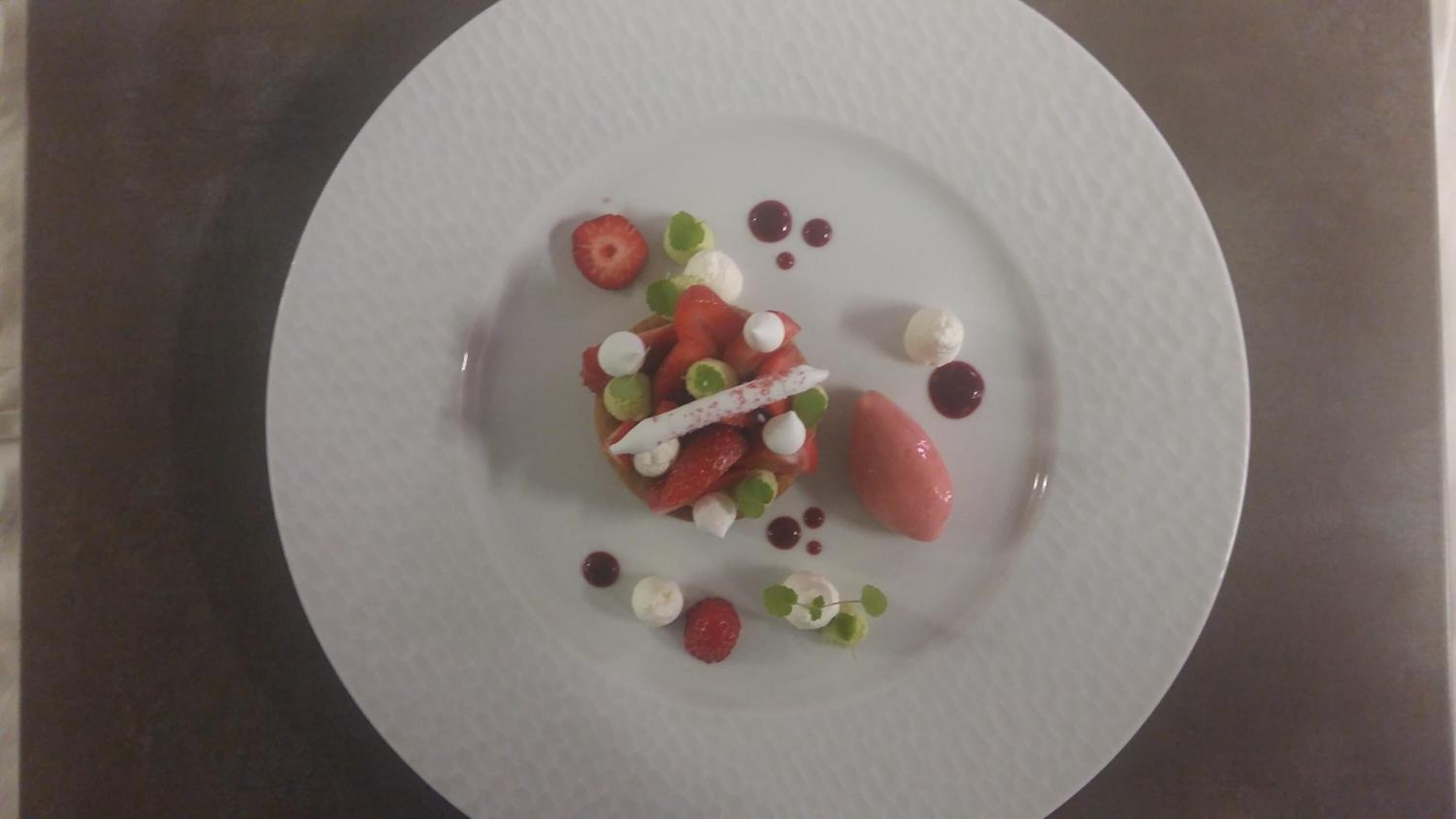 A white plate with a dessert consisting of strawberries, green grapes, and small dollops of cream.