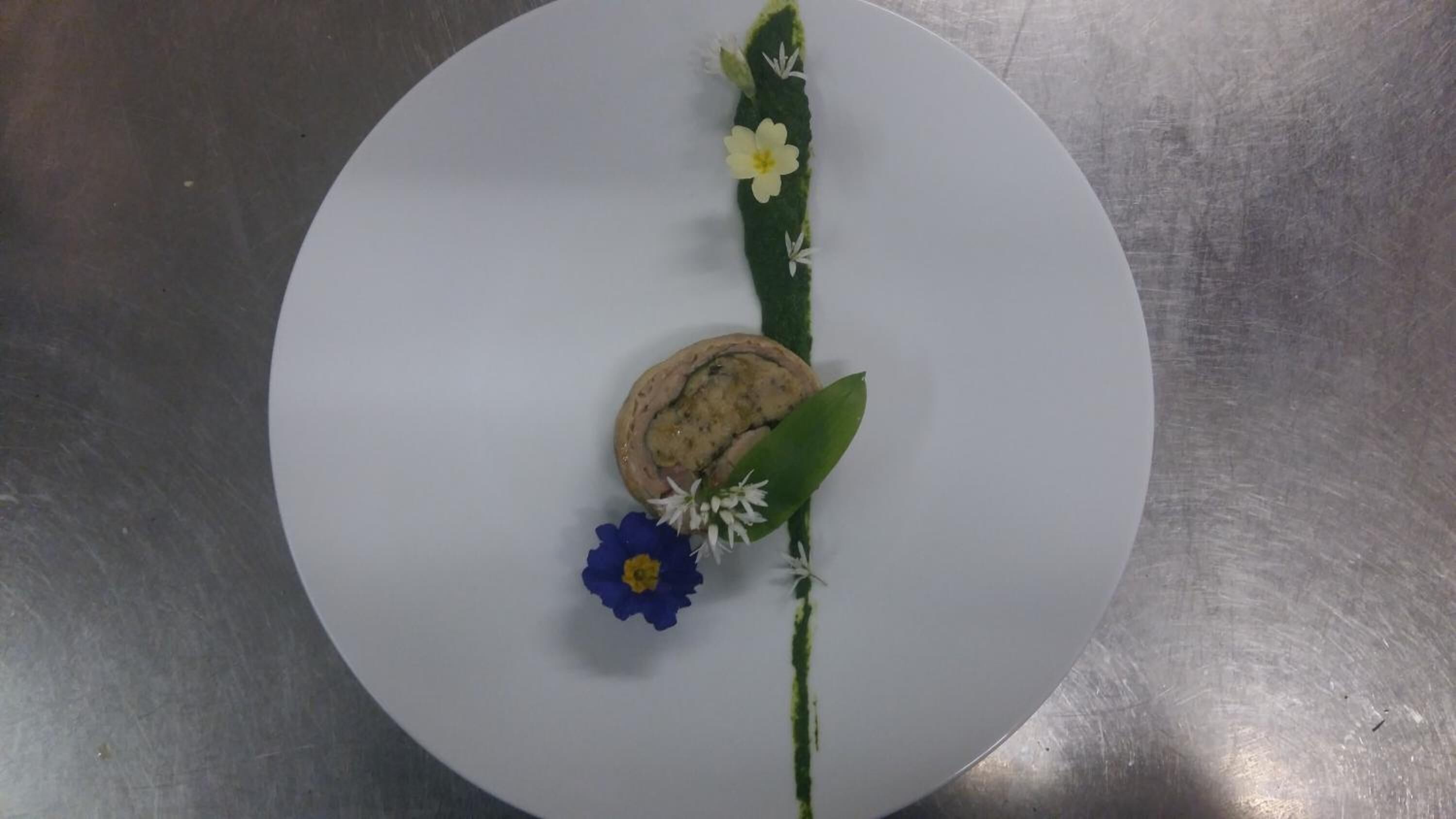 A round white table with a rolled item, possibly a cake, and some flowers.