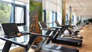 A gym with treadmills, stationary bikes, and a laptop on one of the machines. - QueenSir International Hotel (Xi'an)