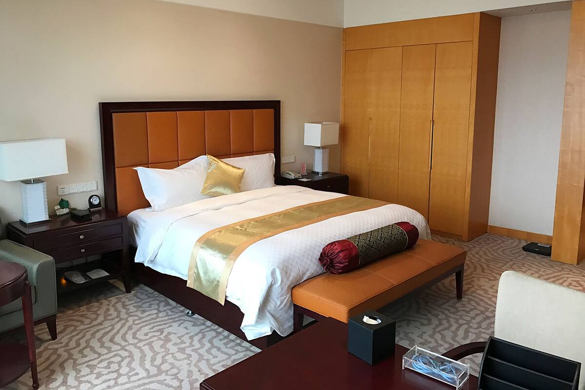 A hotel room with a bed, a nightstand, a desk, a chair, and a wardrobe.