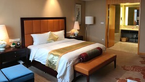 A hotel room with a large bed, bedside lamps, a bench, a nightstand, and a bathroom visible through an open door. - QueenSir International Hotel (Xi'an)