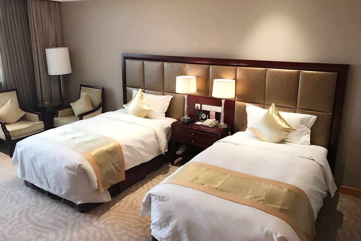 A hotel room with two beds, a nightstand, a lamp, and a chair.