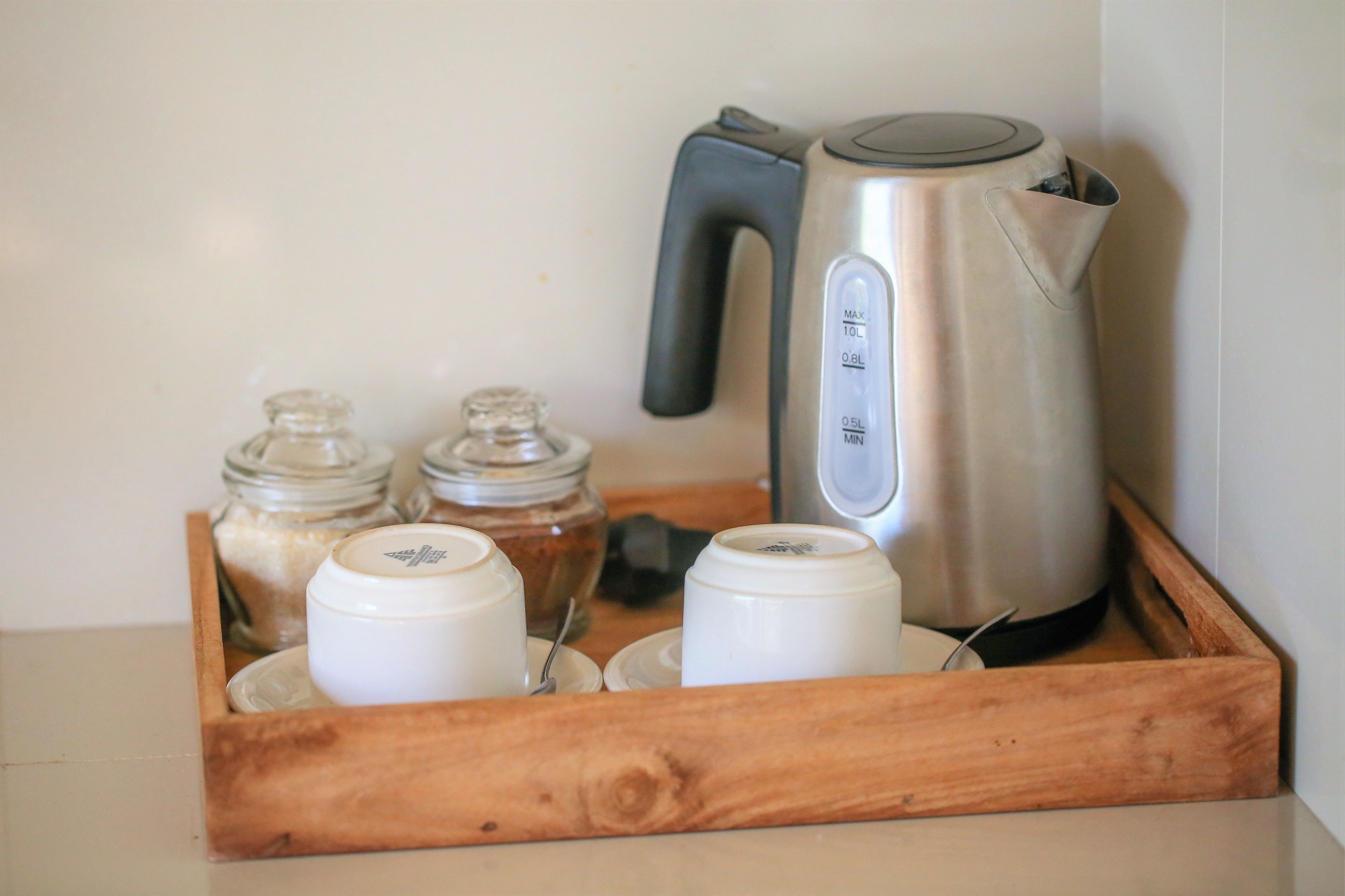 A wooden tray with a kettle, salt and pepper shakers, and two white containers.