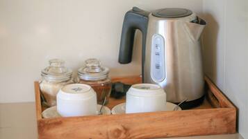 A wooden tray with a kettle, salt and pepper shakers, and two white containers.
