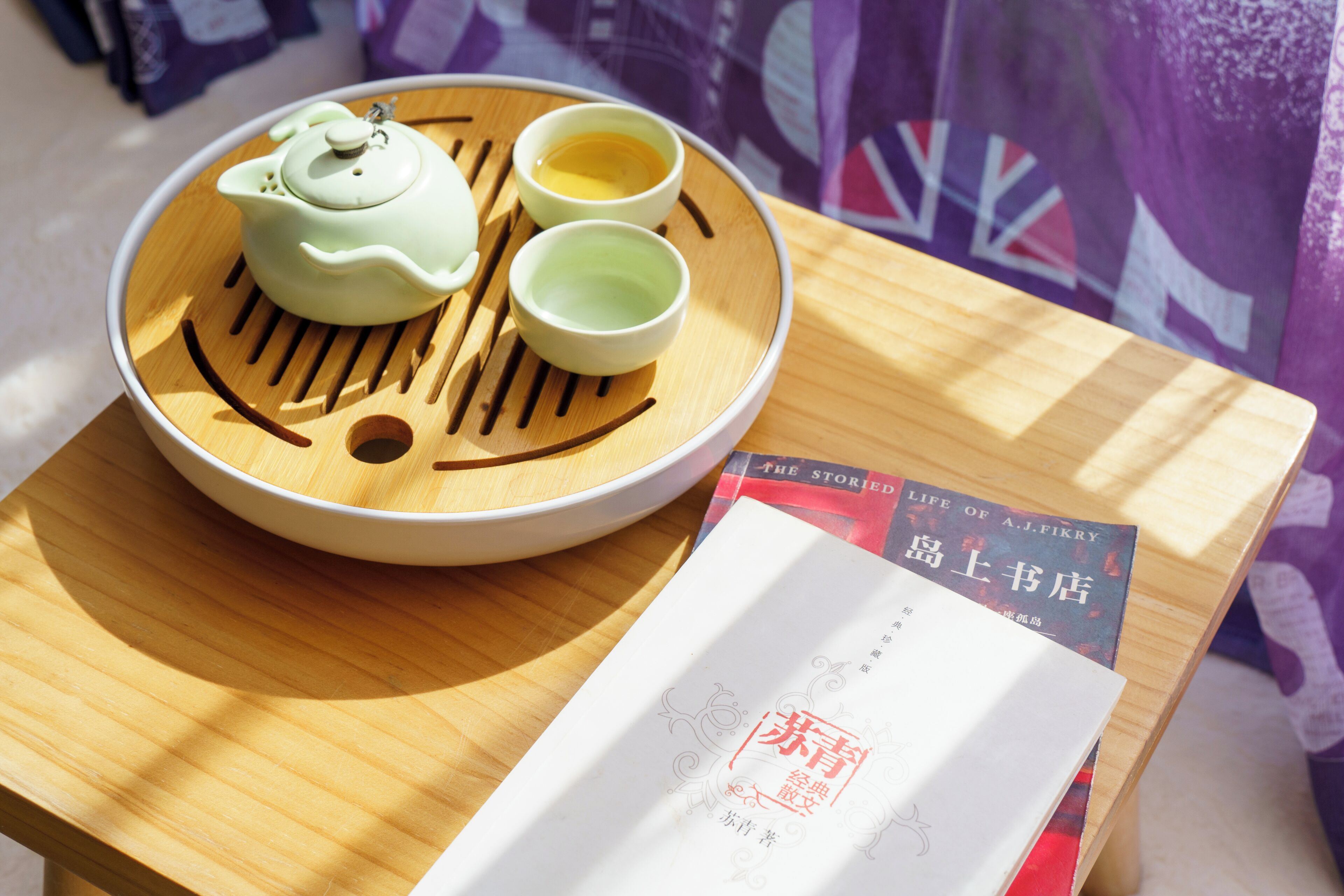 A teapot and two cups on a wooden tray with a smiley face design, placed on a table next to a book.