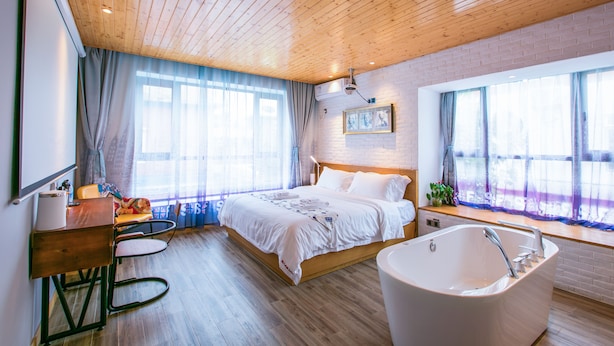 A modern bedroom with a wooden ceiling, a large bed, a bathtub, and a desk with a chair. - Maan Coco Travelling Boutique Inn (Shenzhen)