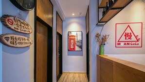 A hallway with a wooden floor, a clock on the left, a 'No Smoking' sign, a 'M A N CoCo' sign, and a red telephone booth poster. - Maan Coco Travelling Boutique Inn (Shenzhen)